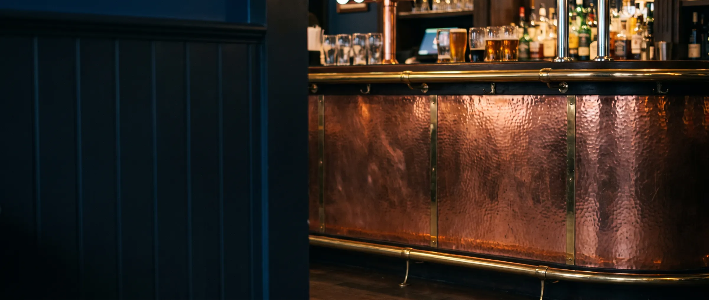 Pub bar counter clad in hammered copper with a brass footrail
