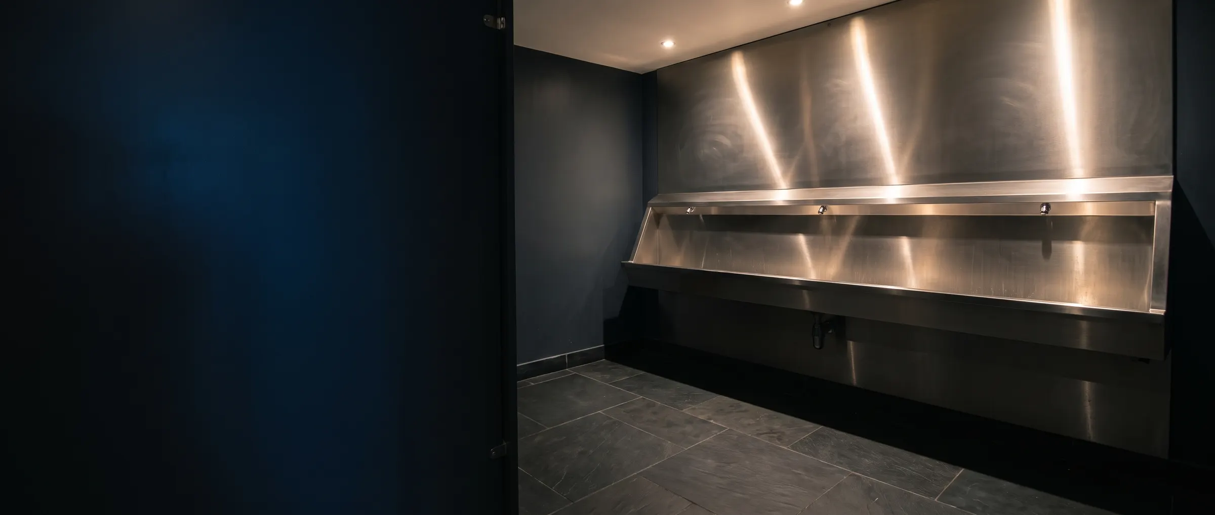 Stainless steel trough urinal in a modern pub washroom